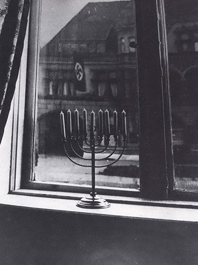 Photograph taken by Rachel, wife of Rabbi Akiva Posner, of their Hanukkah menorah against the backdrop of Nazi flags in Kiel, Germany. 1931