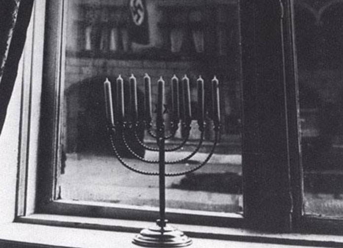 Photograph taken by Rachel, wife of Rabbi Akiva Posner, of their Hanukkah menorah against the backdrop of Nazi flags in Kiel, Germany. 1931